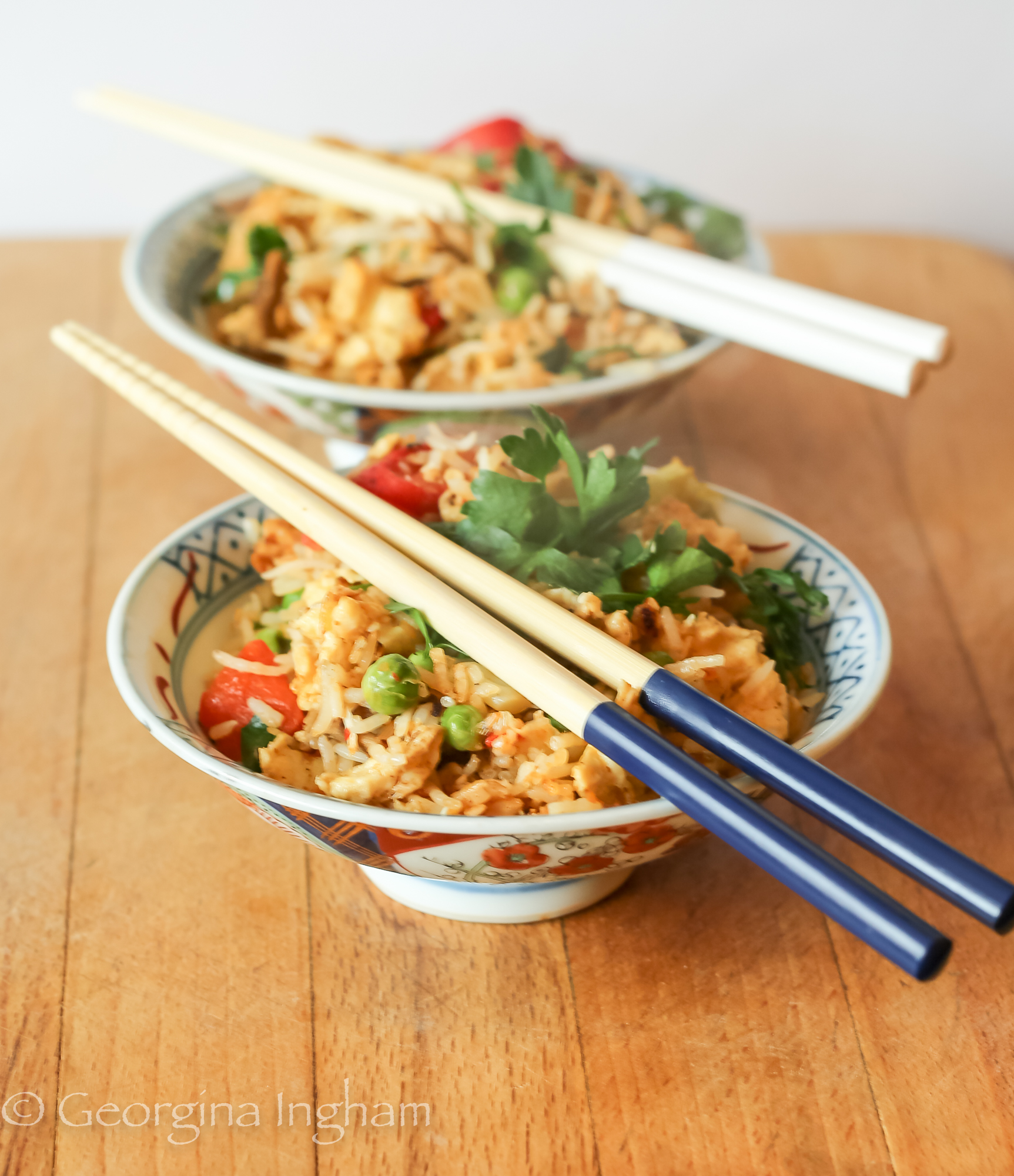 Two bowls of homemade Yangzhou fried rice with prawns, egg, peas and red pepper, served with chopsticks on a wooden table